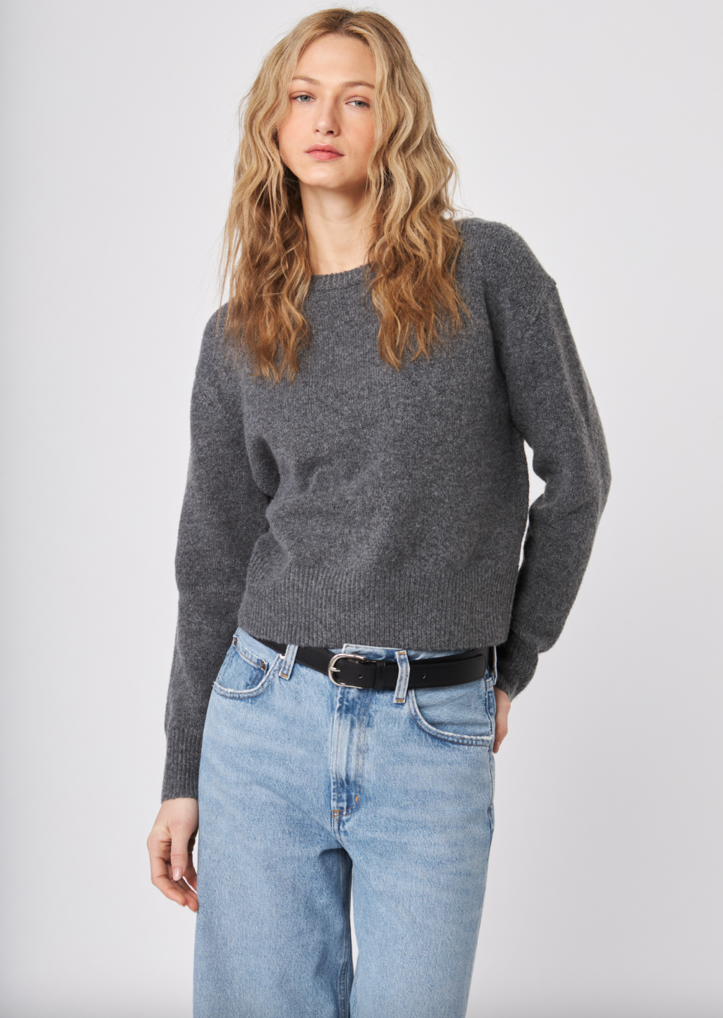 Woman wearing a gray sweater and blue jeans against a white background — alternate view