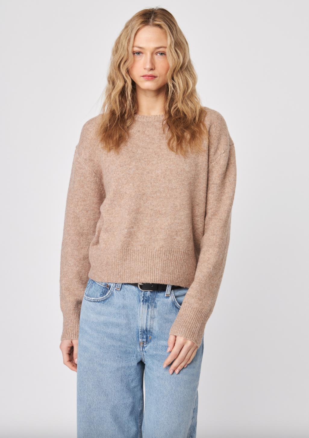 Woman wearing a beige sweater and light blue jeans against a white background — alternate view